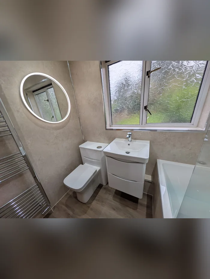 Family bathroom with beige stone-effect panels, a round LED mirror, white vanity unit and bath
