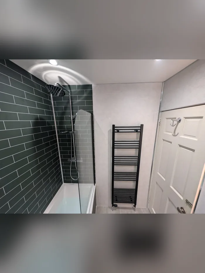 Shower over bath with dark green metro tiles, a rainfall shower head and a black towel rail