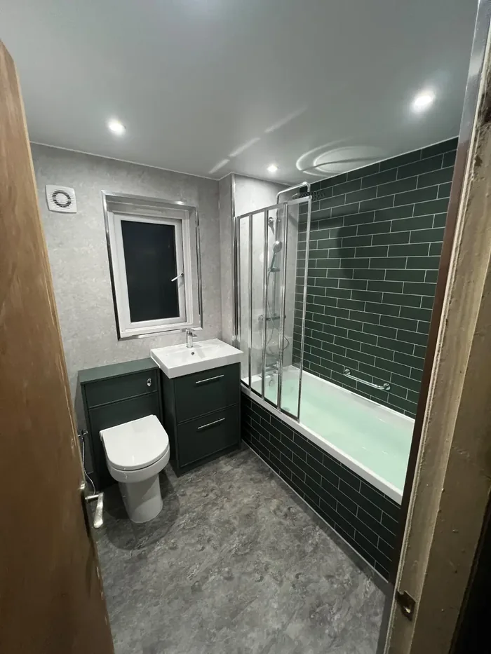 Whole bathroom with a green metro tiled bath, folding screen, dark green vanity unit and grey marble panels