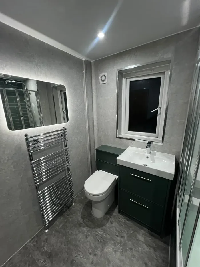 Grey marble-effect wall panels with a dark green vanity and toilet unit, LED mirror and chrome towel rail