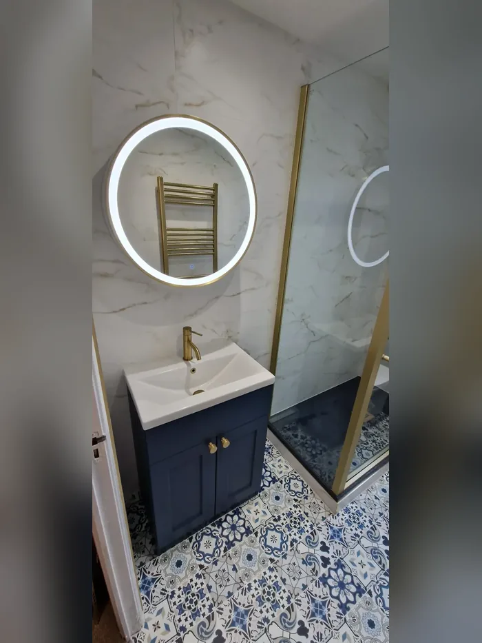 Navy vanity unit with a brushed brass tap under a round LED mirror, with blue and white patterned floor tiles