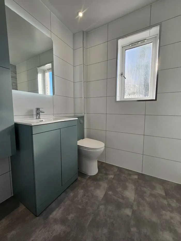 Sage green vanity unit and toilet with an LED mirror and large format white wall tiles