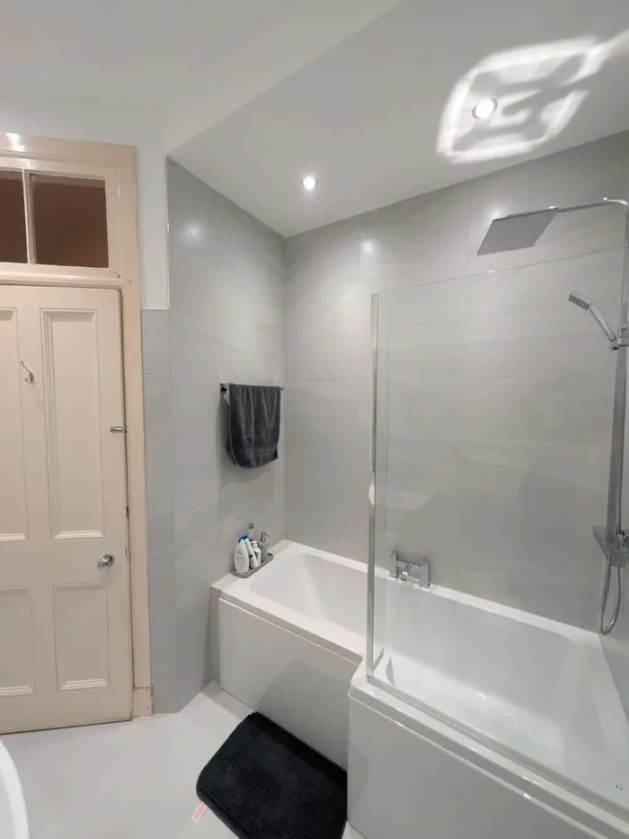 Shower bath with a glass screen in light grey tiles, beside a panelled period door with a fanlight