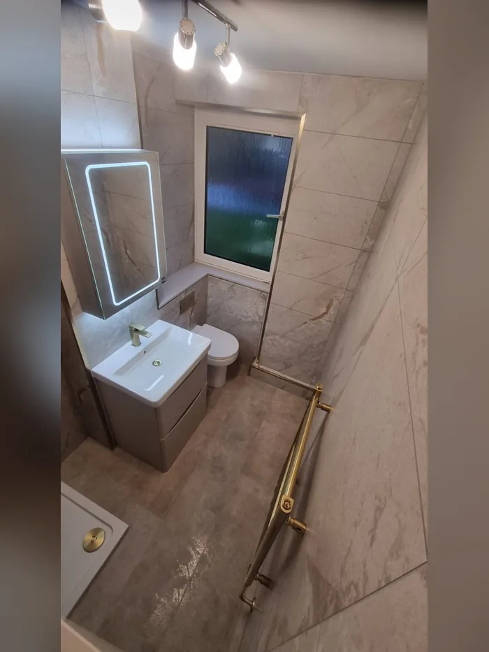 En-suite with beige marble-effect tiles, brass trims, an LED mirror cabinet and grey vanity unit