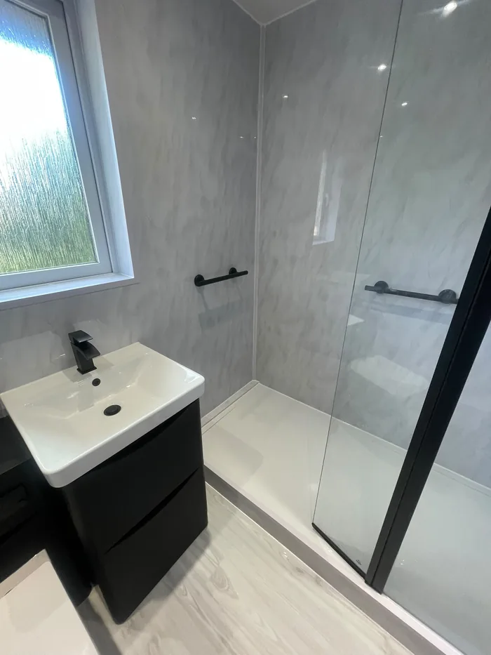 Shower room with light grey marble-effect panels, a black vanity unit, black tap and black grab rail