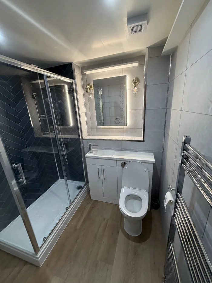Shower room with navy herringbone tiles in the enclosure, a white vanity and WC unit and a backlit mirror
