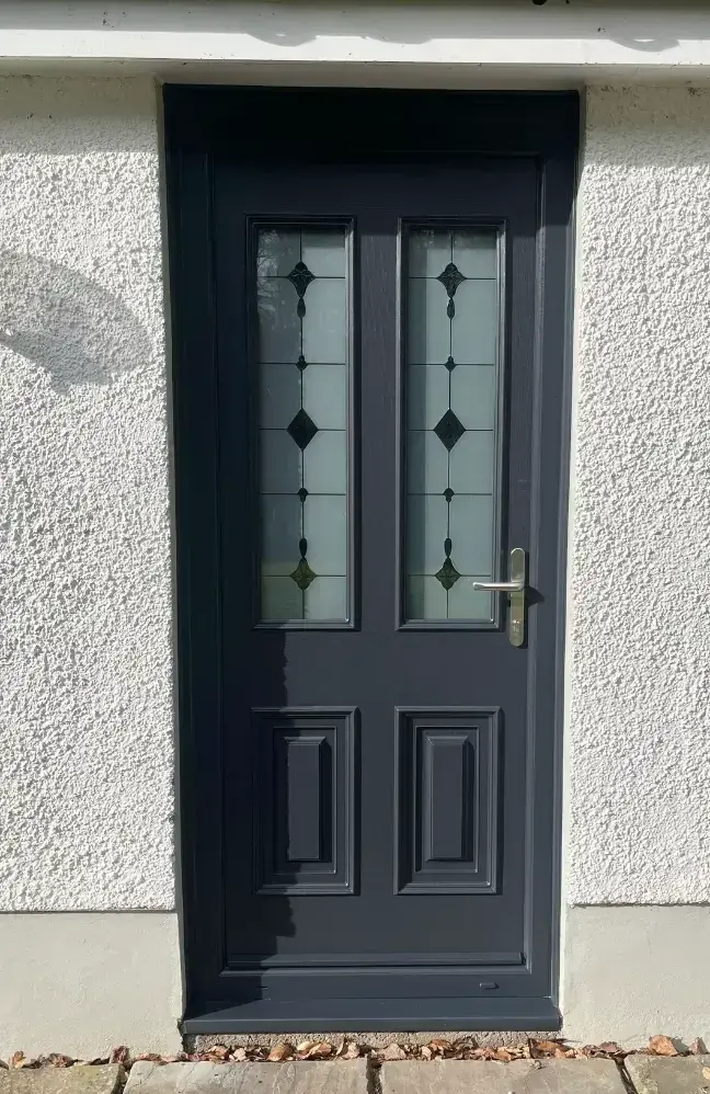Dark grey composite front door with two tall diamond-leaded glass panels, fitted in a roughcast house
