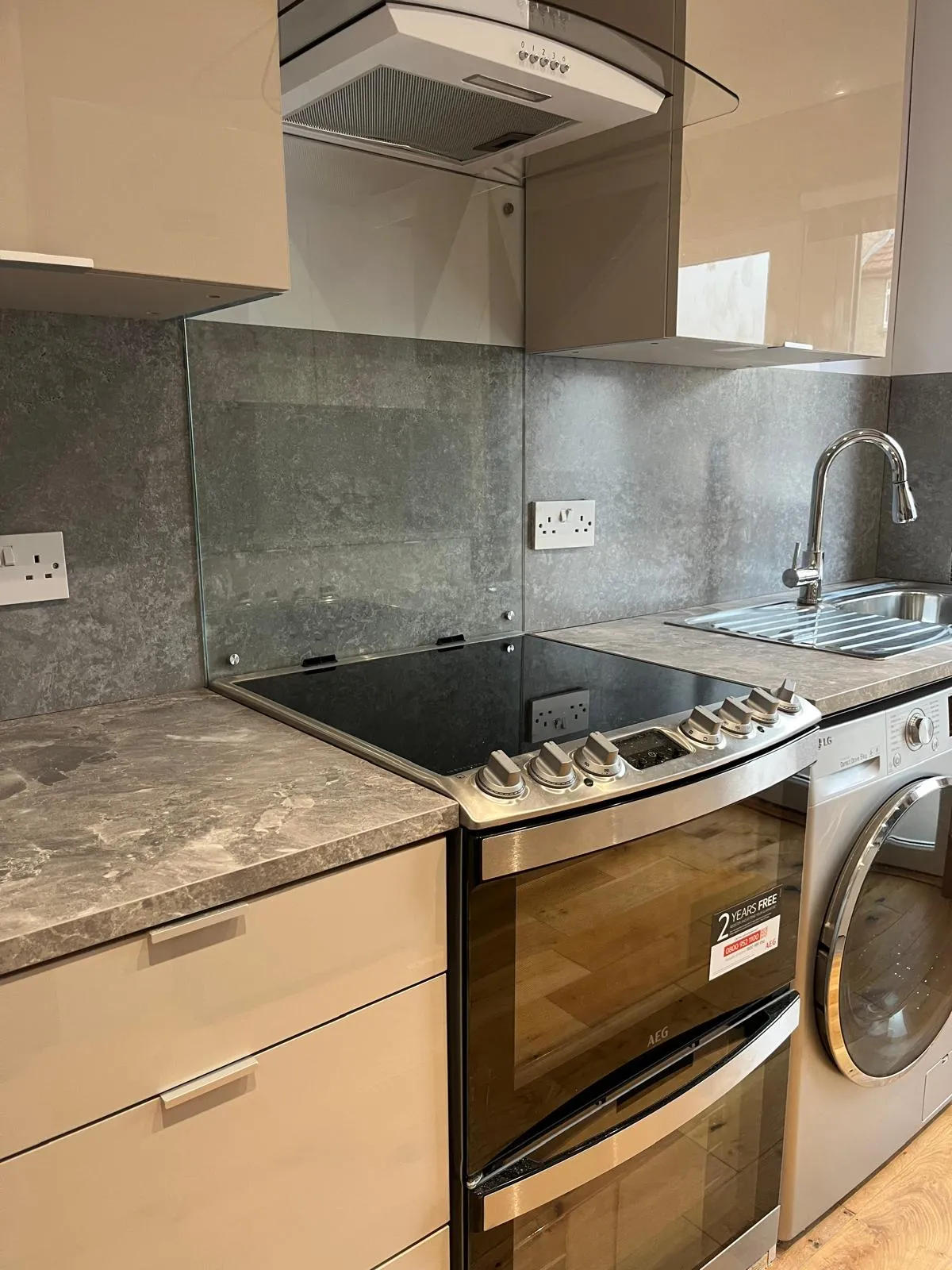 Cream gloss kitchen with chimney hood and glass splashback by Ultimate Home Solutions