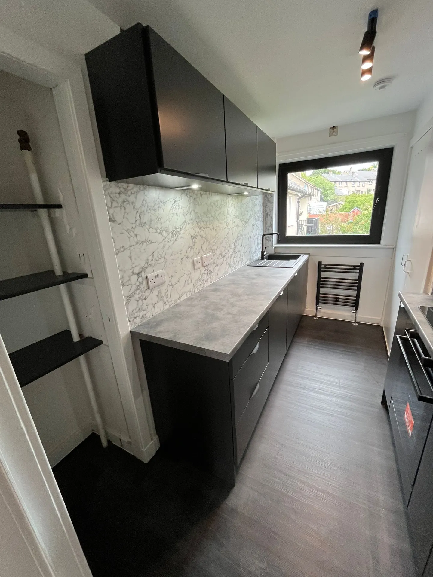 Matte black galley kitchen with marble-effect splashback by Ultimate Home Solutions