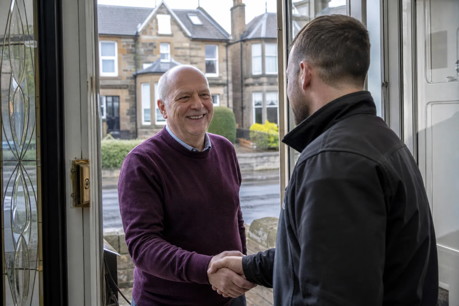 A homeowner and a fitter shaking hands at the door after a roof replacement